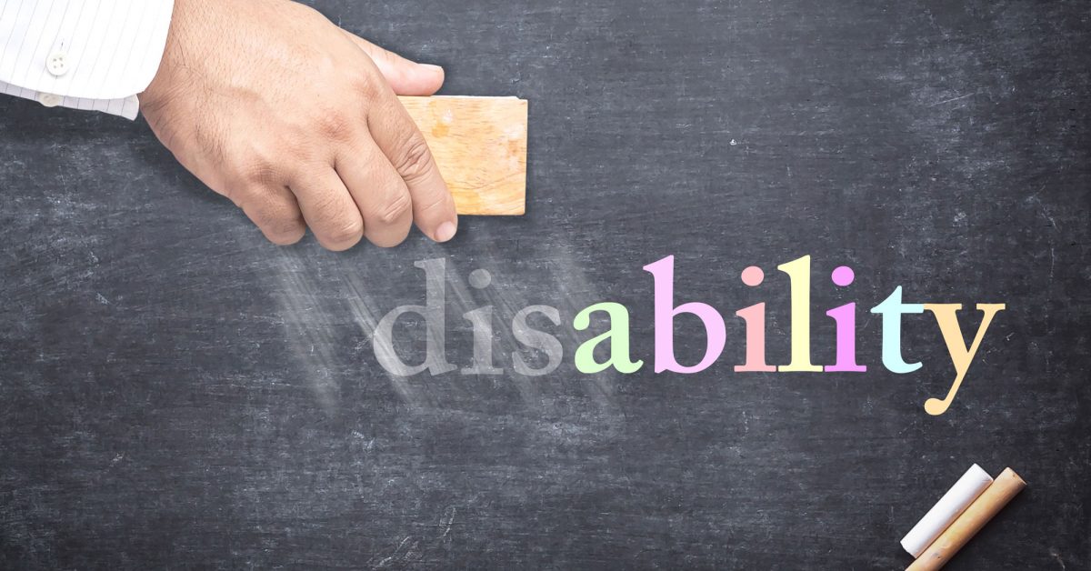 A hand erasing the dis from the word disability, which is written on a chalkboard