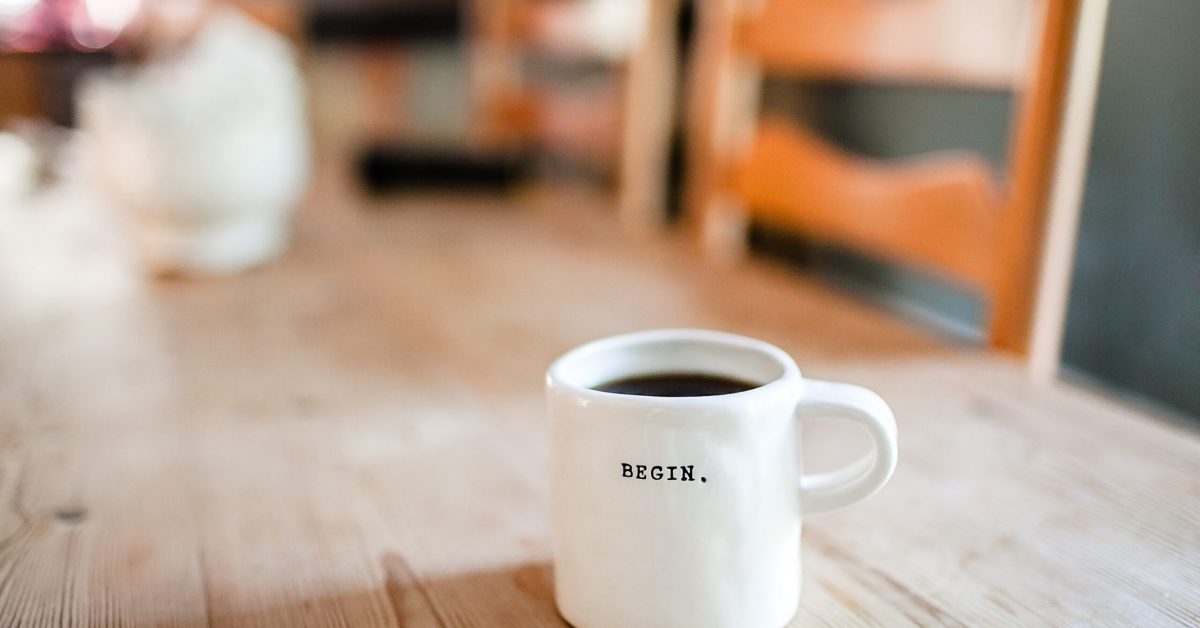 A full coffee cup basking in beautiful natural light from a window, with the word Begin